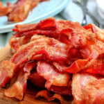 air fryer bacon piled high on wood board with blue plate in the background square