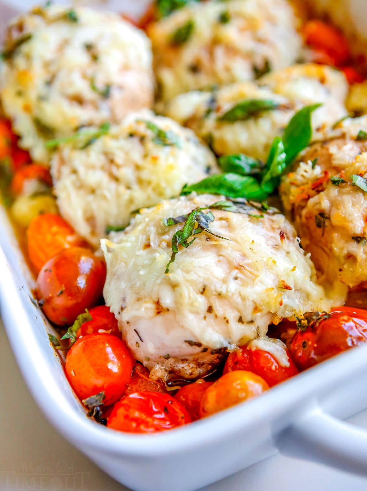 baked chicken in white casserole dish with cheese tomatoes and basil