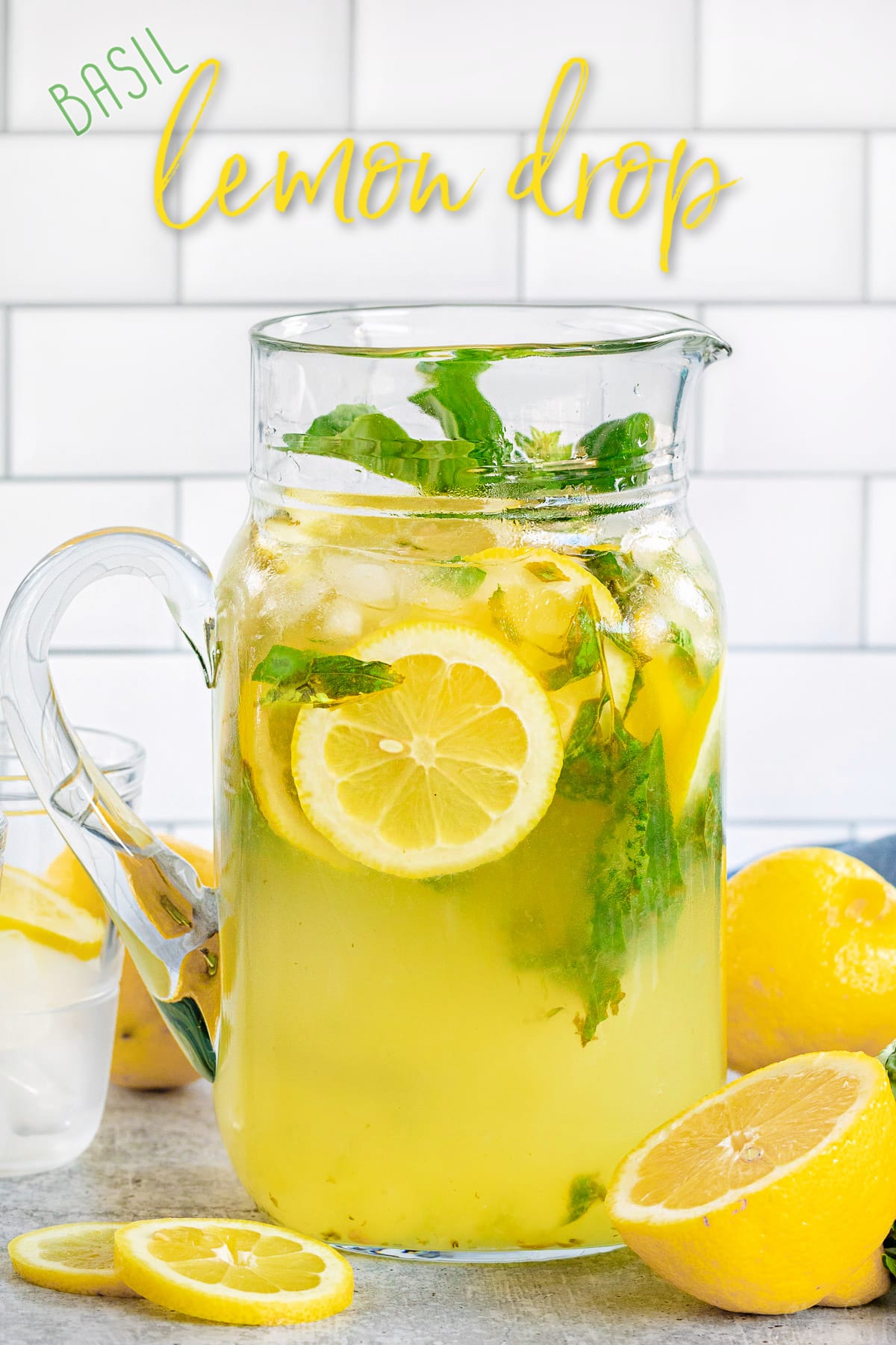 basil lemon drop in glass pitcher with lemon slices in and around pitcher with title overlay