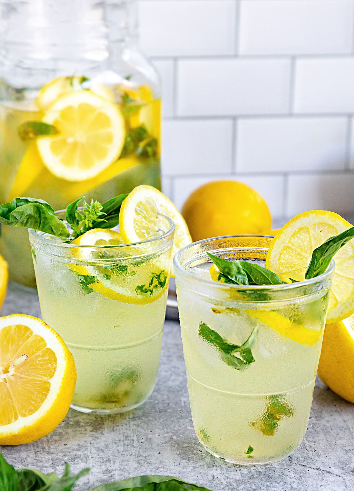 basil lemon drop poured into two glasses with fresh basil and halved lemons table