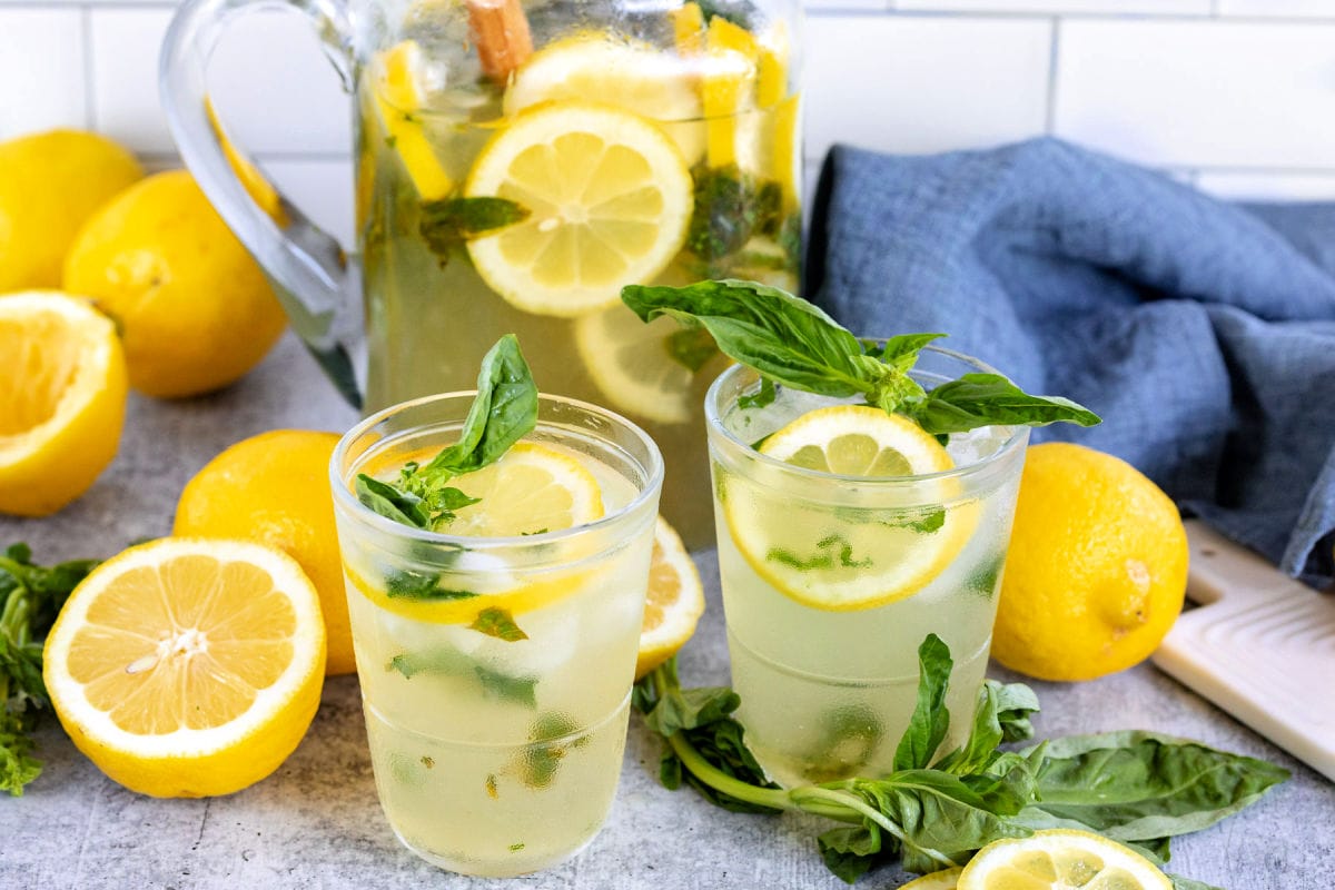 basil lemon drop poured into two glasses with pitcher in the background with basil and lemons scattered about