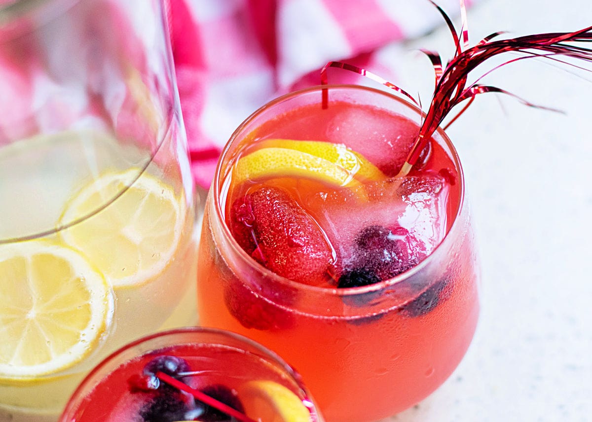 berry lemonade recipe in 2 glasses with lemonade in pitcher on the side