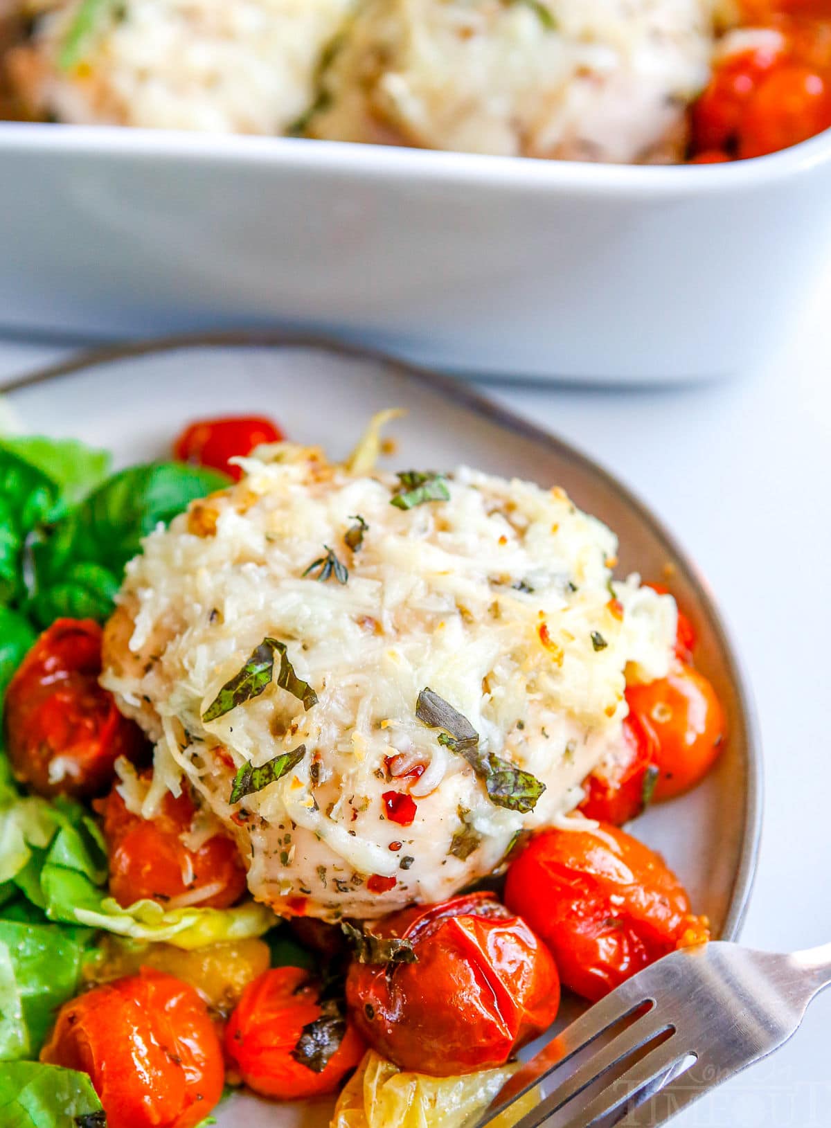 chicken and tomatoes on plate with side salad with casserole dish in background