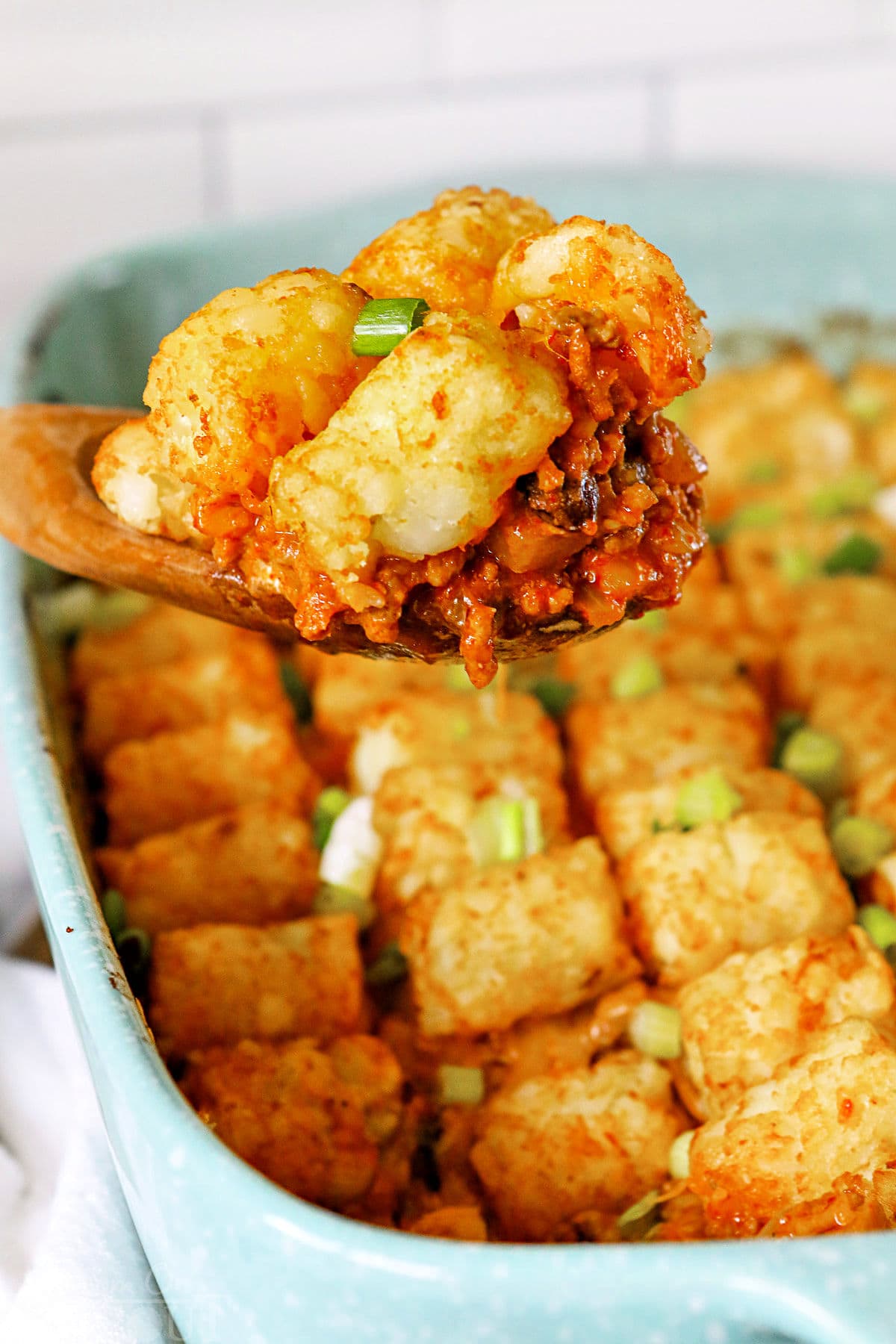 taco tater tot casserole being scooped out of dish with large wood spoon