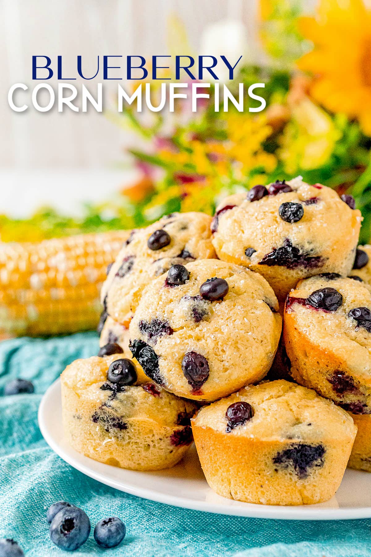 blueberry corn muffins piled high on white plate sitting on blue napkin with text overlay