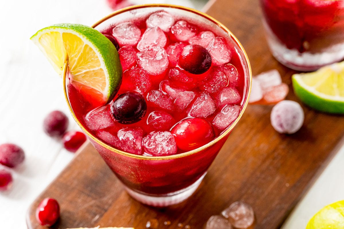 vodka cranberry cocktail in glass with lime wedge and cranberries sitting on dark wood board