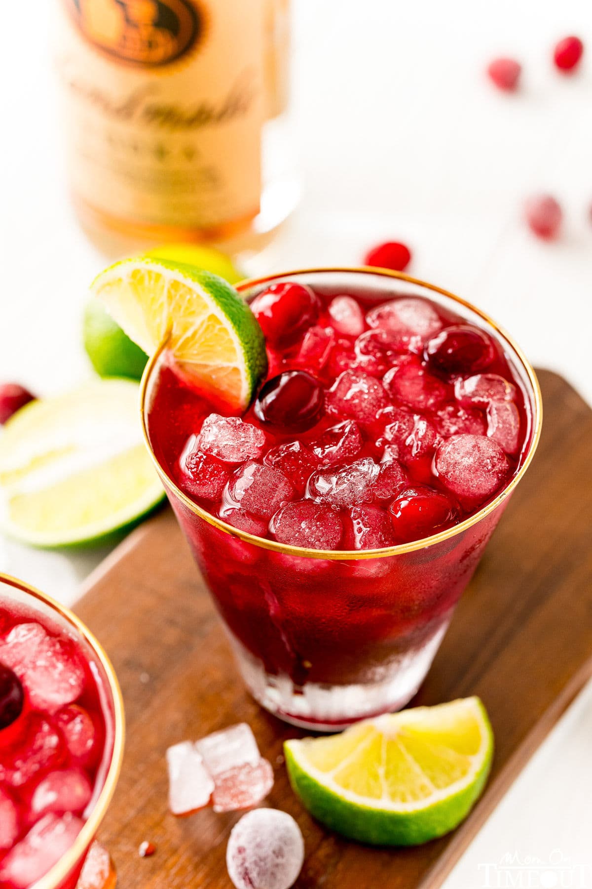 vodka cranberry cocktail in glass with lime wedge and cranberries sitting on dark wood board