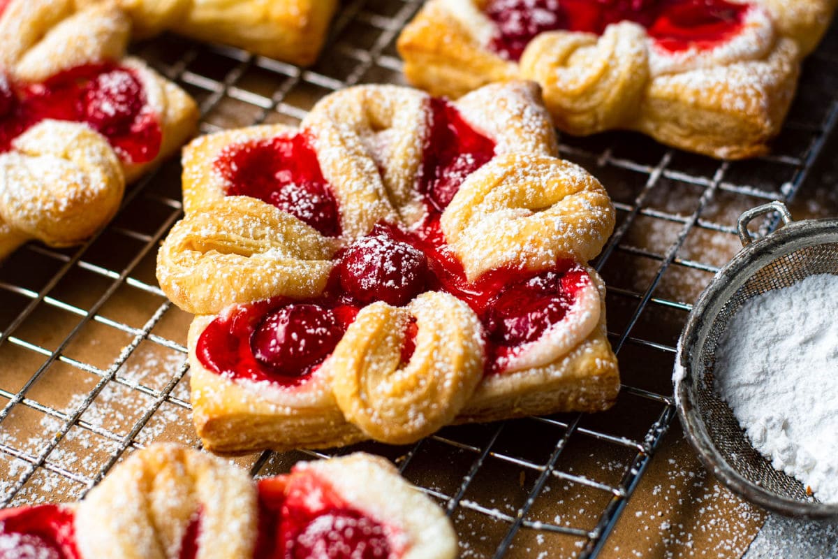 cheese danish with cherries baked and sprinkled with powdered sugar sitting on wire cooling rack