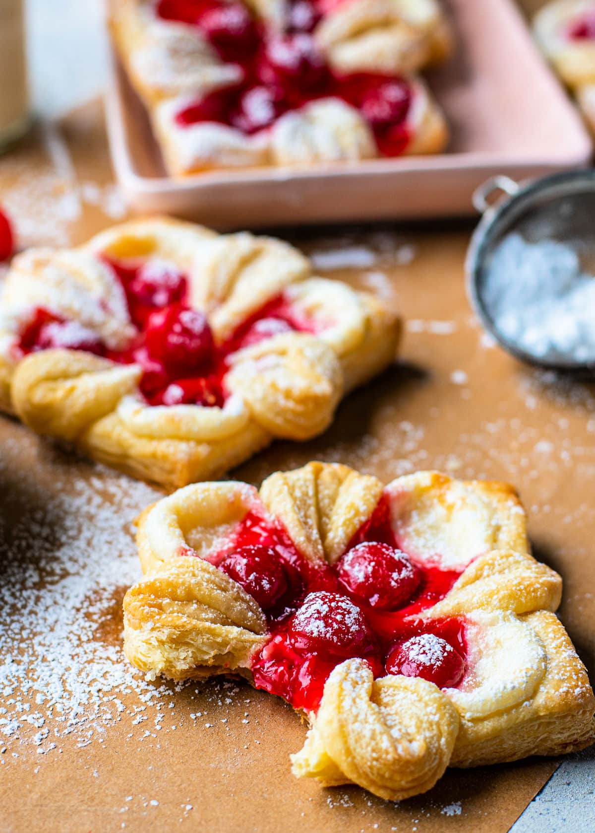 cherry danish with bite taken on brown parchment paper and danishes in the background