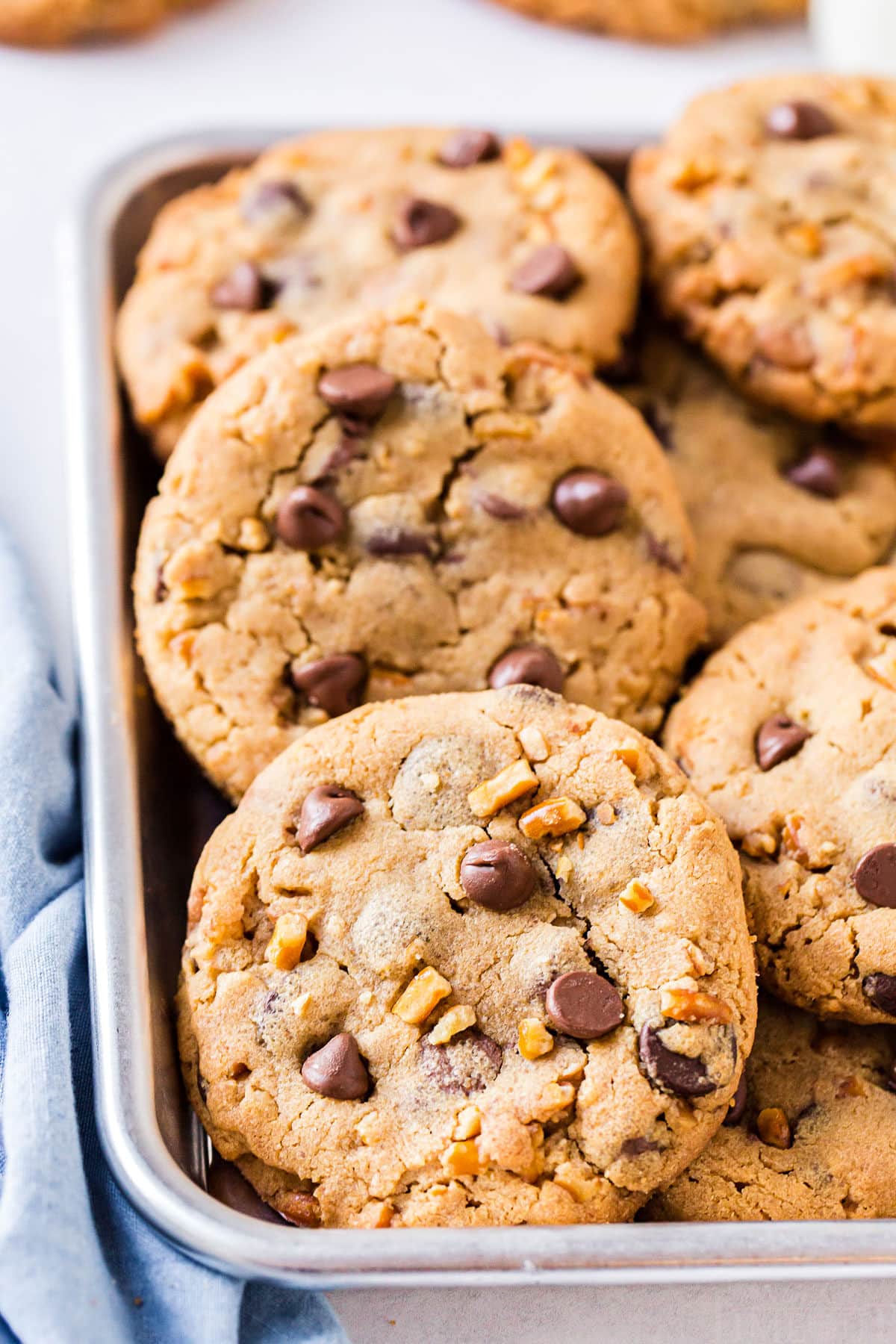 chocolate chip cookies piled in small silver tray with blue napkin on the side
