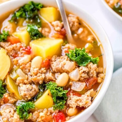 close up view of sausage kale white bean soup in white bowl with a spoon in it