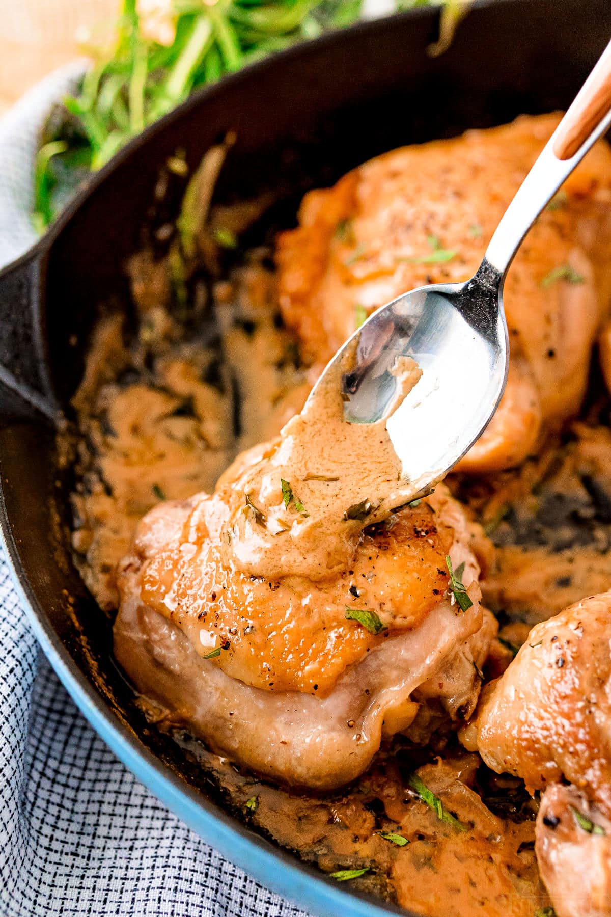 mustard sauce being spooned onto chicken thigh in skillet