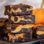 Brownies de calabaza apilados de 4 en 4 sobre tabla de madera oscura con calabaza de fondo