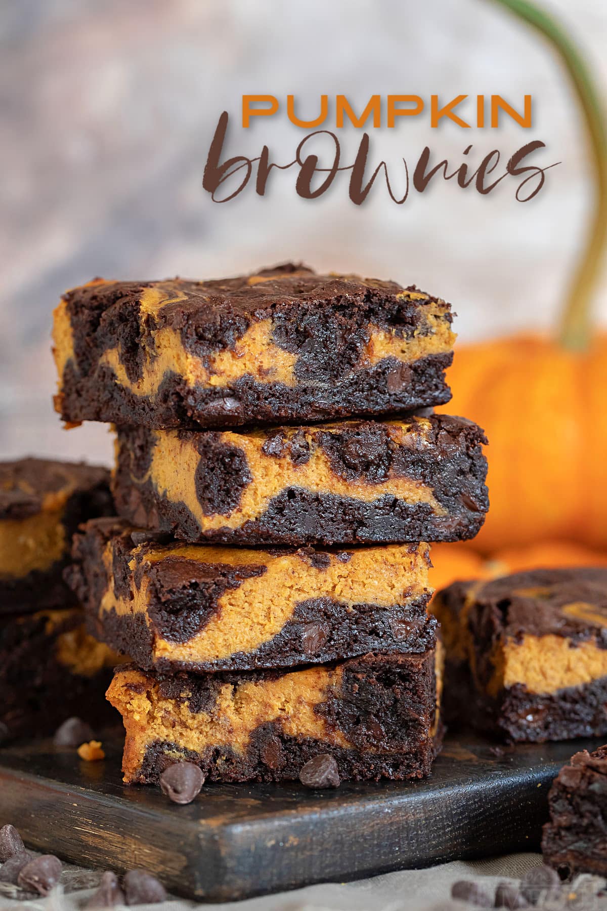 pumpkin brownies ułożone 4 wysoko na desce z ciemnego drewna z dynią w tle i z nałożonym tekstem