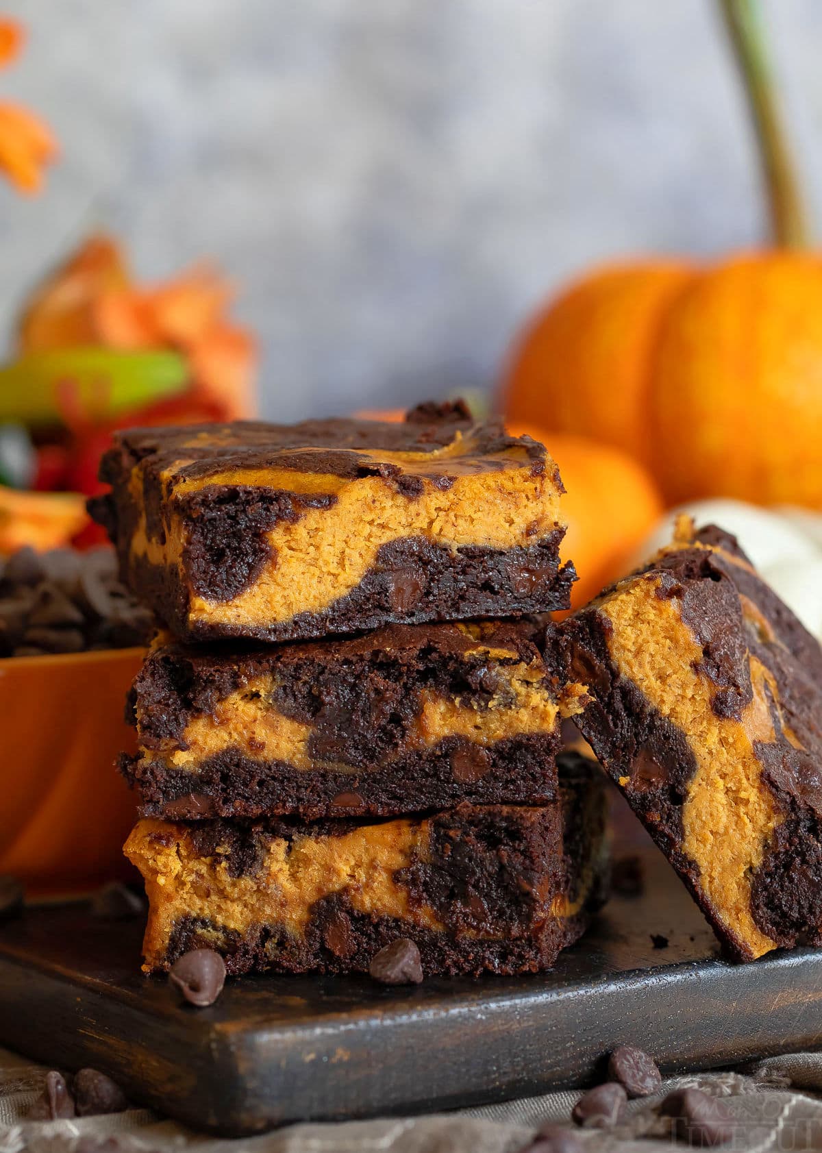 pumpkin brownies ułożone po trzy na desce z ciemnego drewna z dynią w tle