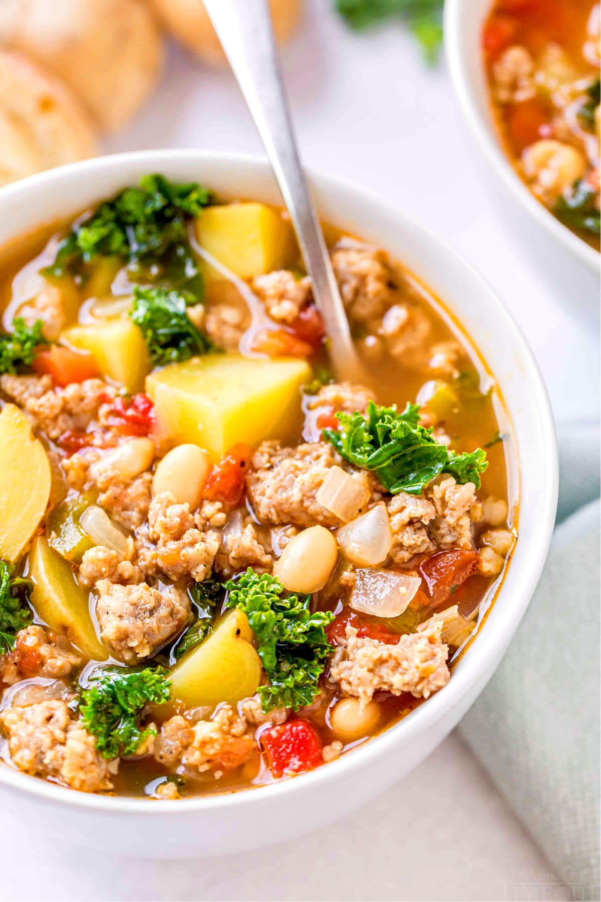 close up view of sausage kale white bean soup in white bowl with a spoon in it