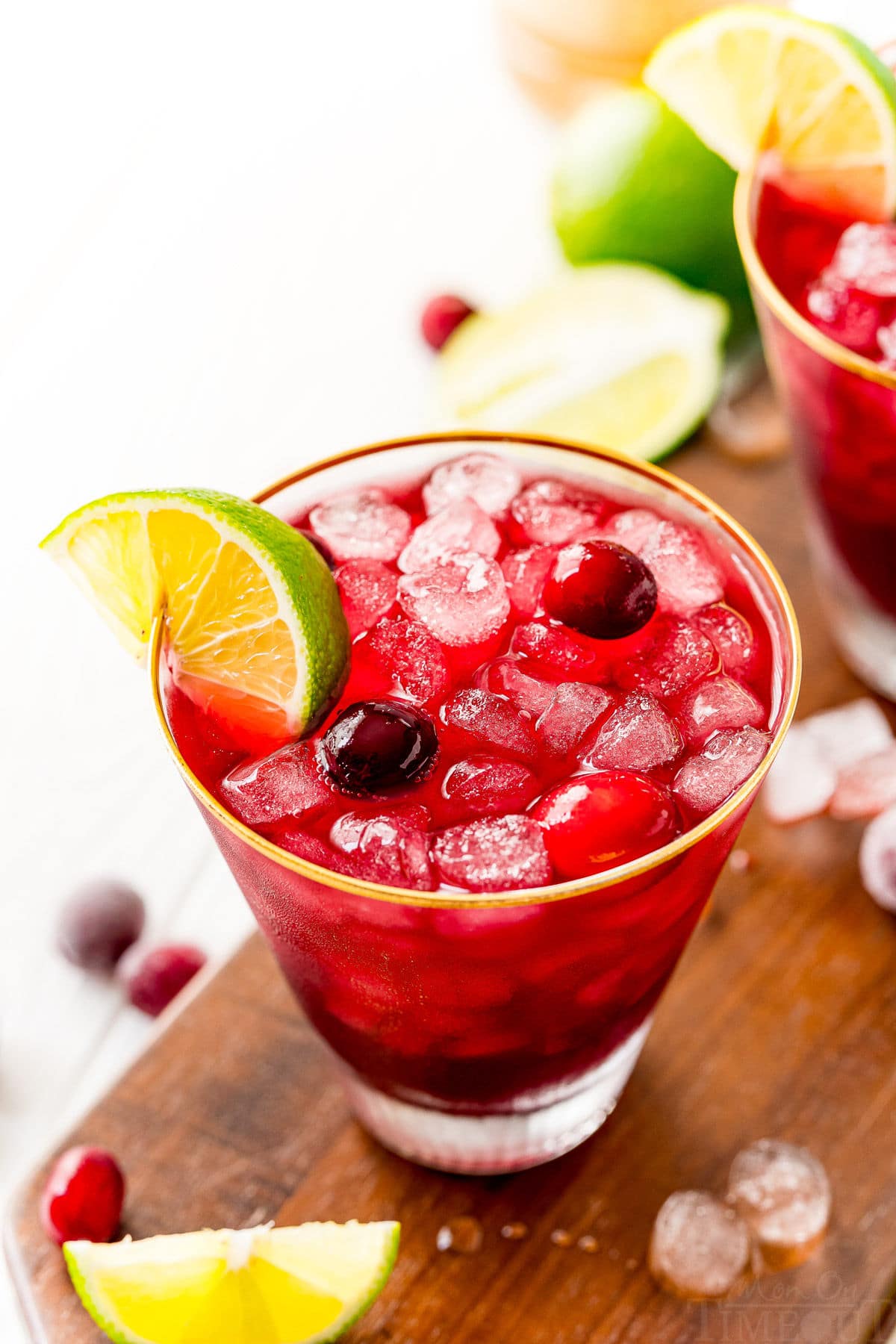 vodka cranberry cocktail in glass with lime wedge and cranberries sitting on dark wood board