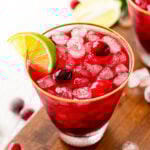 vodka cranberry cocktail in glass with lime wedge and cranberries sitting on dark wood board