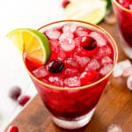 vodka cranberry cocktail in glass with lime wedge and cranberries sitting on dark wood board