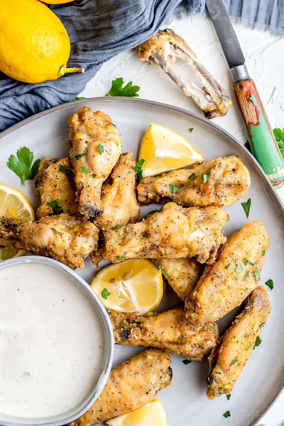 baked chicken wings on plate with ranch in small bowl and garnished with parsley and lemon top down view