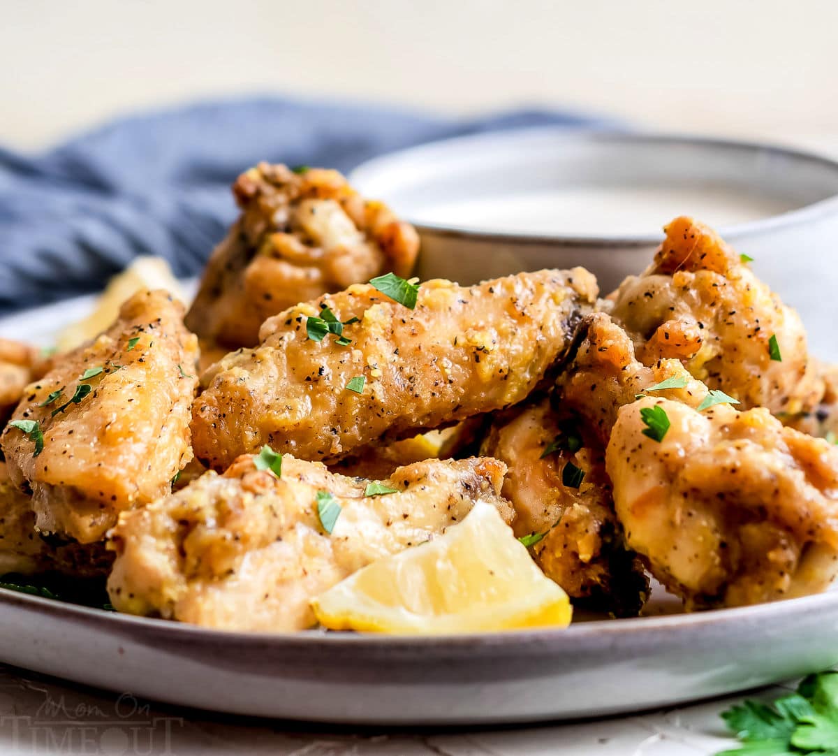 front view of baked chicken wings on plate with lemon wedges and blue napkin in the background