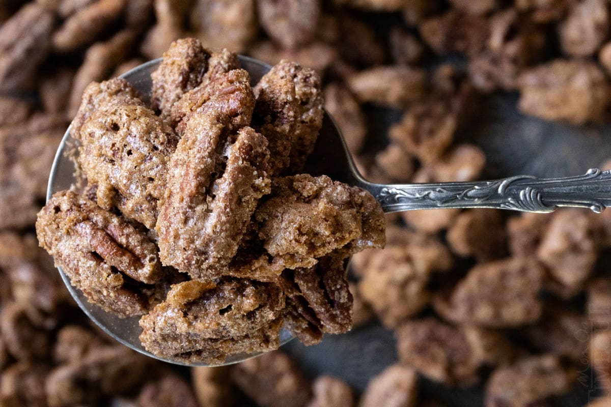candied pecans scooped up on spoon with a sheet pan underneath covered with more pecans