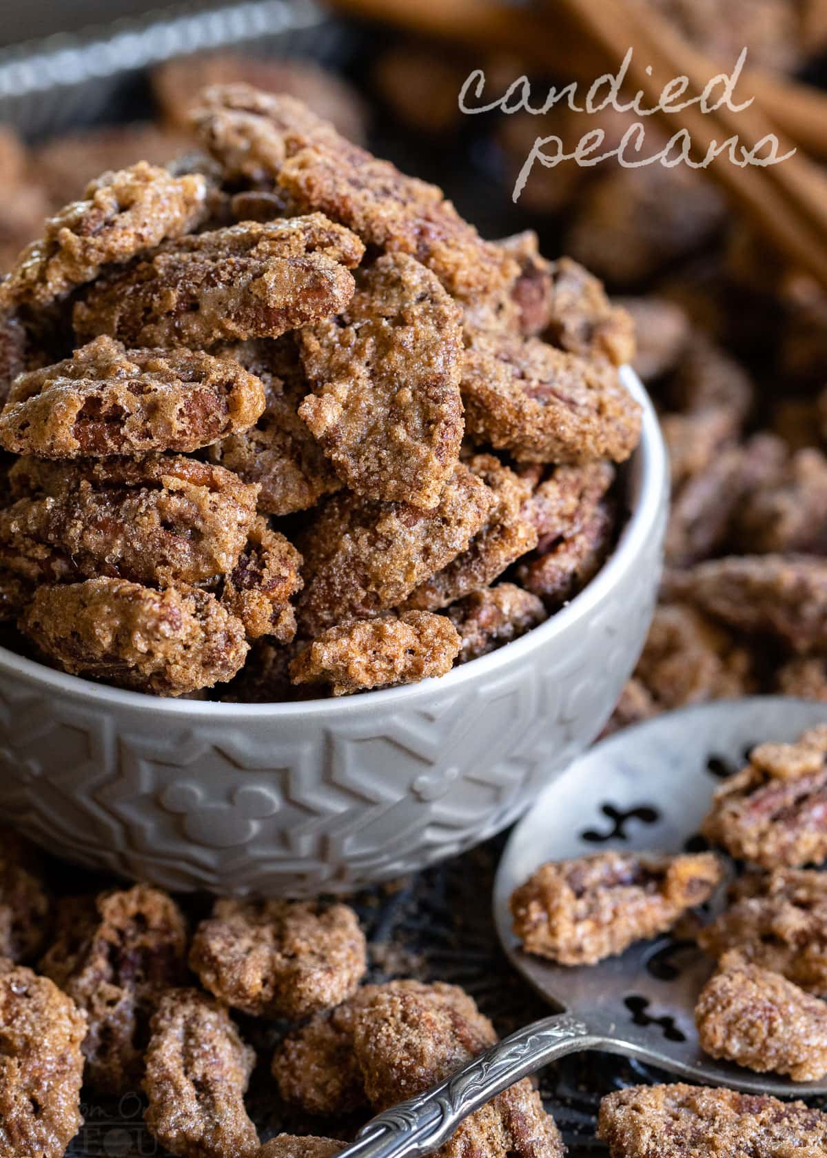 candied pecans in small gray bowl sitting on baking sheet with more pecans title overlay in upper right corner