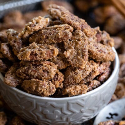 candied pecans in small gray bowl on baking sheet with more pecans