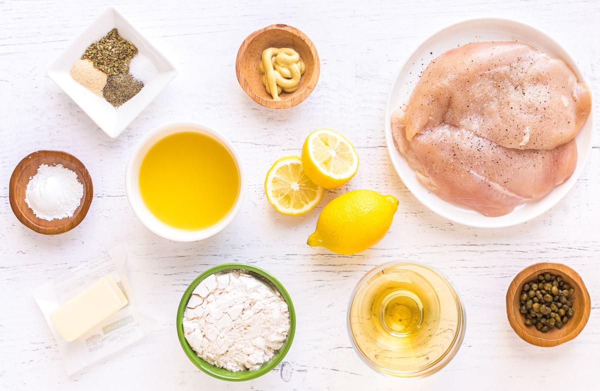 chicken piccata ingredients set out in small bowls and plates on white surface.