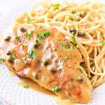 easy chicken piccata recipe plated on a white plate with spaghetti and garnished with parsley.
