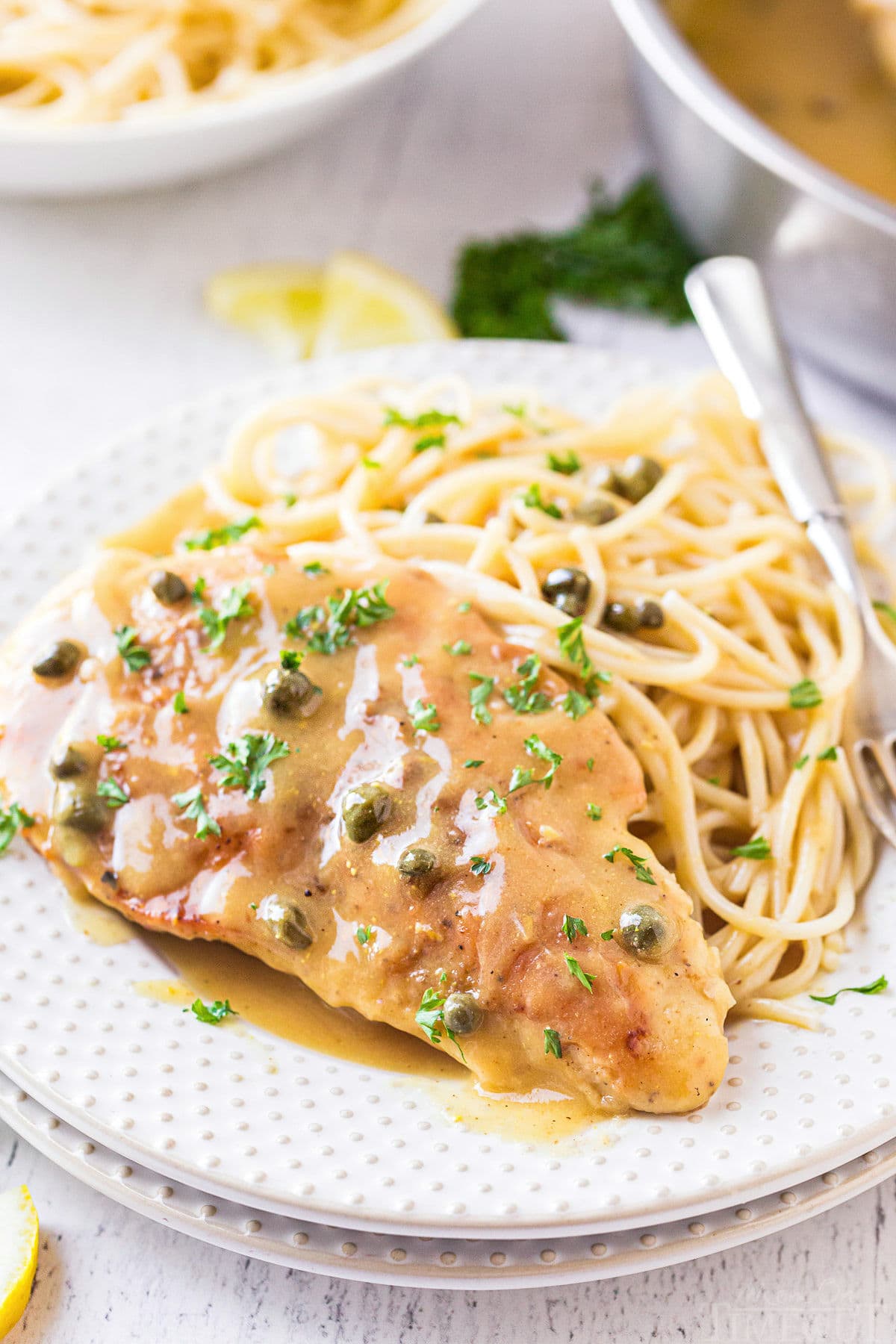 chicken piccata plated with pasta on a white plate and topped with fresh parsley.