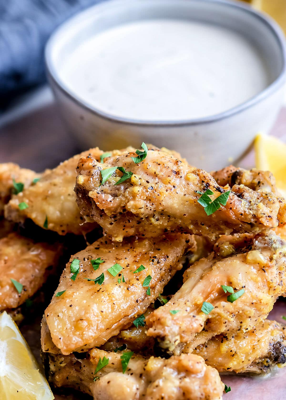 crispy baked chicken wings garnished with lemon pepper sauce and parsley small bowl of ranch in back