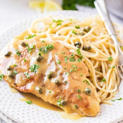 easy chicken piccata recipe plated on a white plate with spaghetti and garnished with parsley