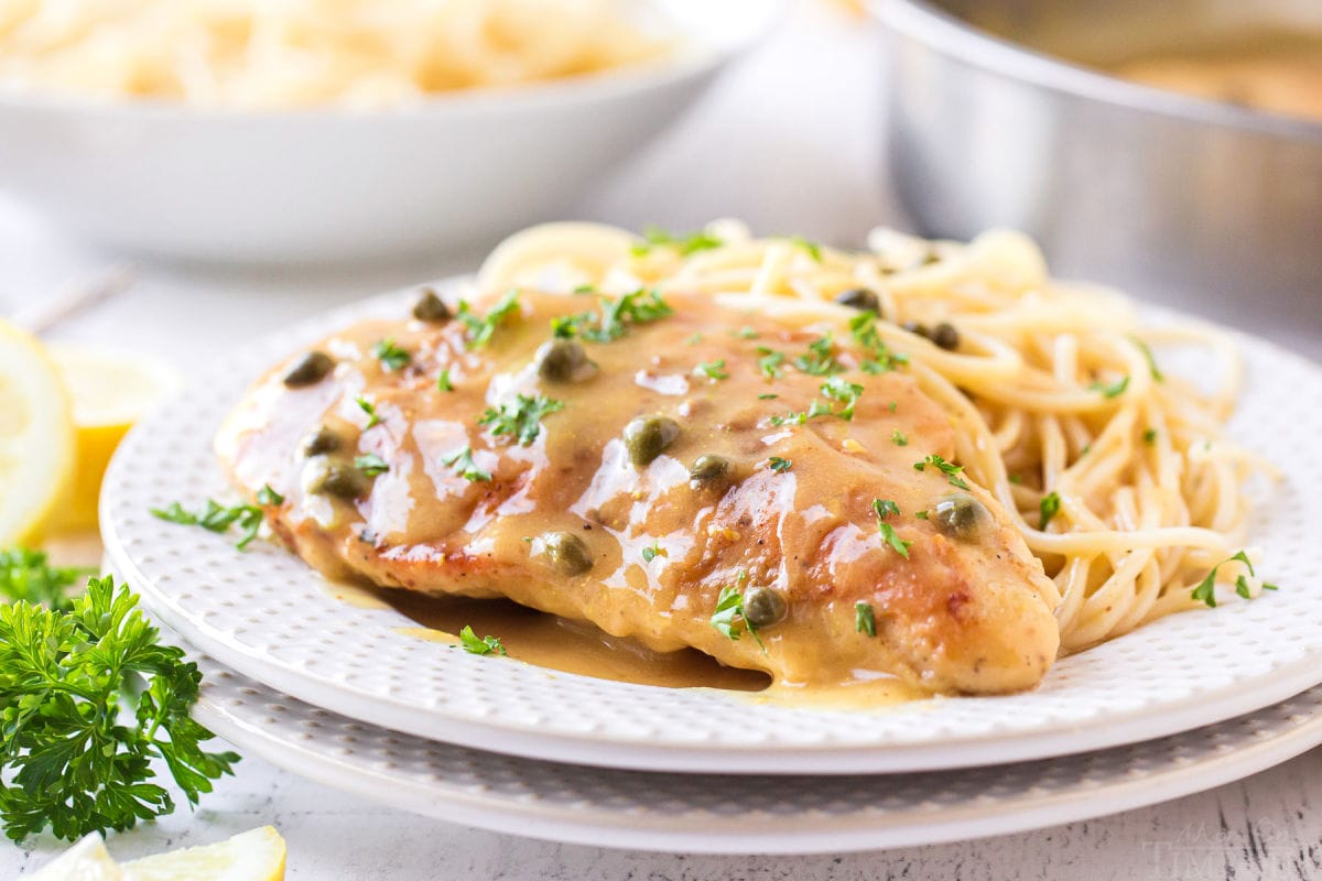 lemon chicken piccata recipe on white plate with spaghetti on the side and parsley garnish