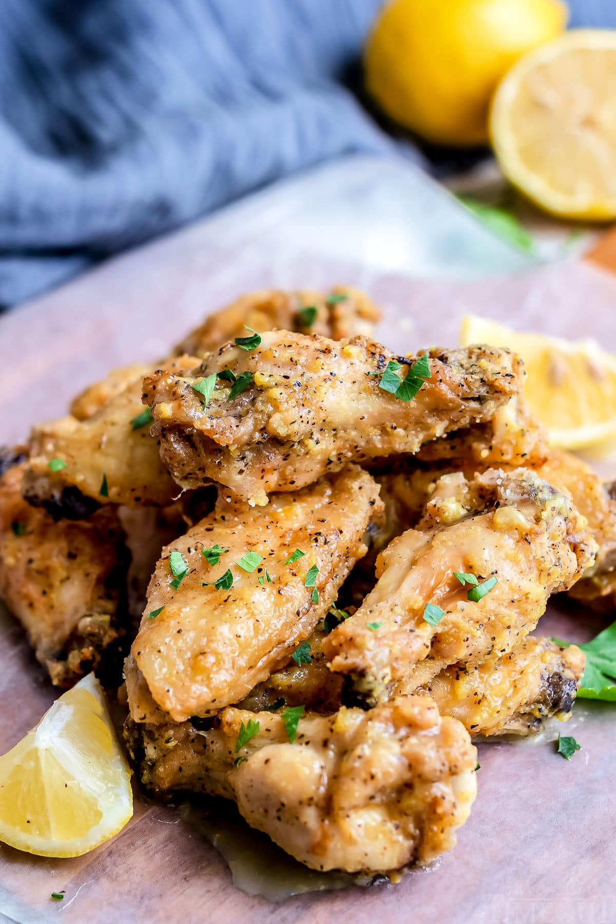 lemon pepper wings stacked in a pile with a blue napkin in the back with cut lemons