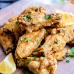 lemon pepper wings stacked in a pile garnished with parsley and lemon wedges sitting on parchment paper