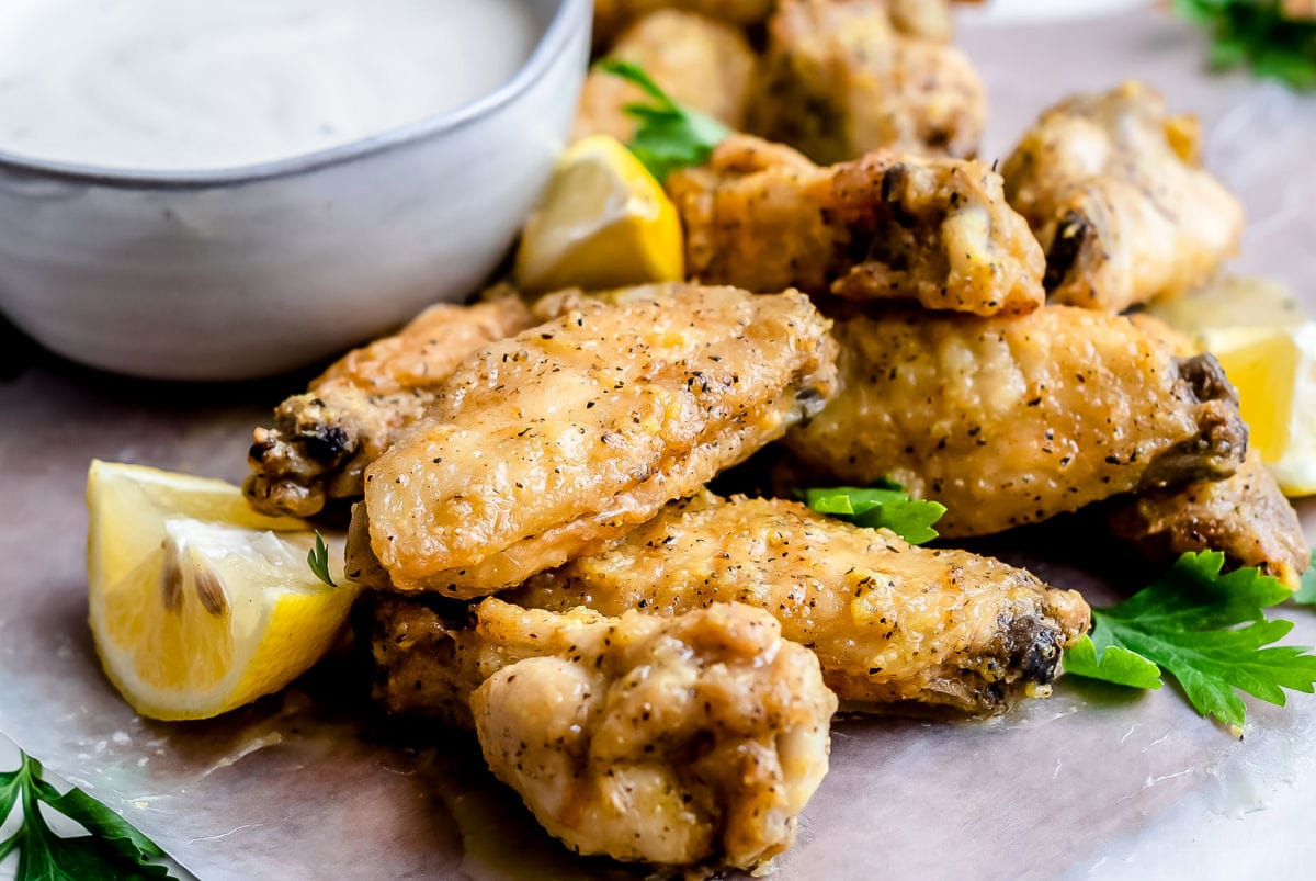 front view of baked chicken wings on gray plate garnished with chopped parsley and small bowl of ranch in background