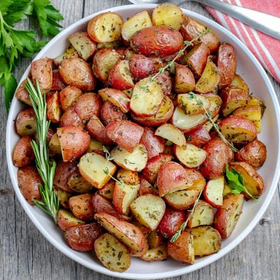 white plate with roasted potatoes garnished with fresh herbs and red towel underneath