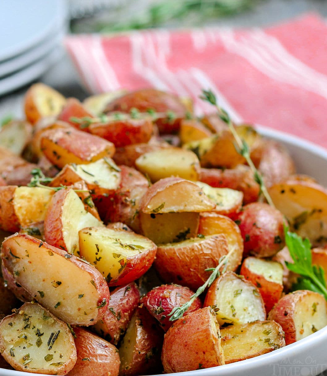 roasted potatoes recipe close up in white bowl with stack of plates in background