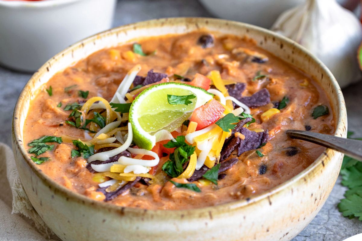 close up chicken enchilada soup in bowl with toppings and lime wedge