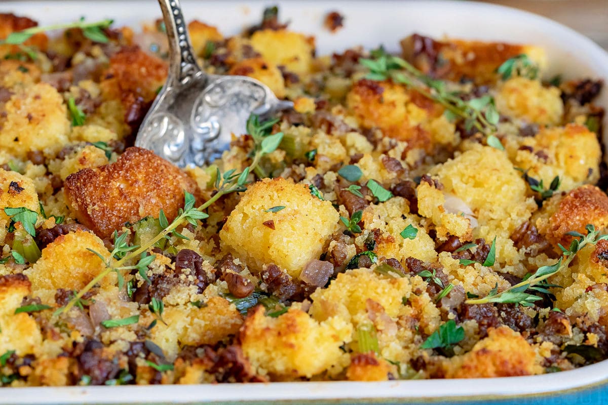 cornbread stuffing close up in casserole dish with antique spoon ready to scoop out a serving