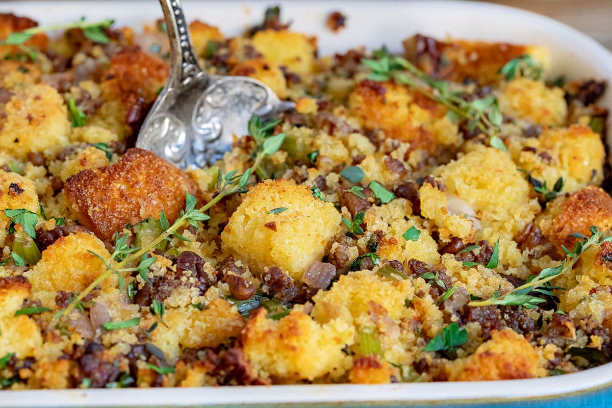 cornbread stuffing close up in casserole dish with antique spoon ready to scoop out a serving