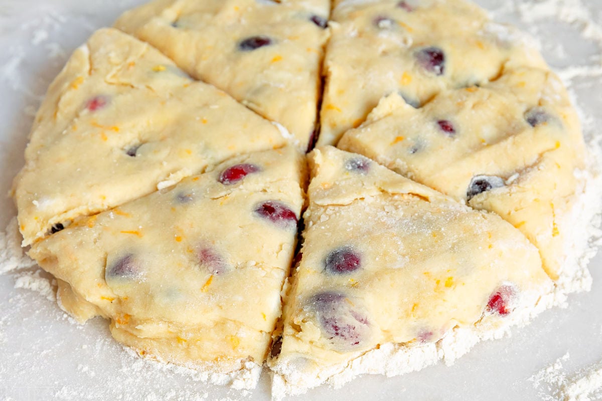 cranberry orange scones dough cut into wedges on marble surface