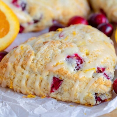 cranberry orange scone sitting on parchment paper with orange glaze drizzled on top