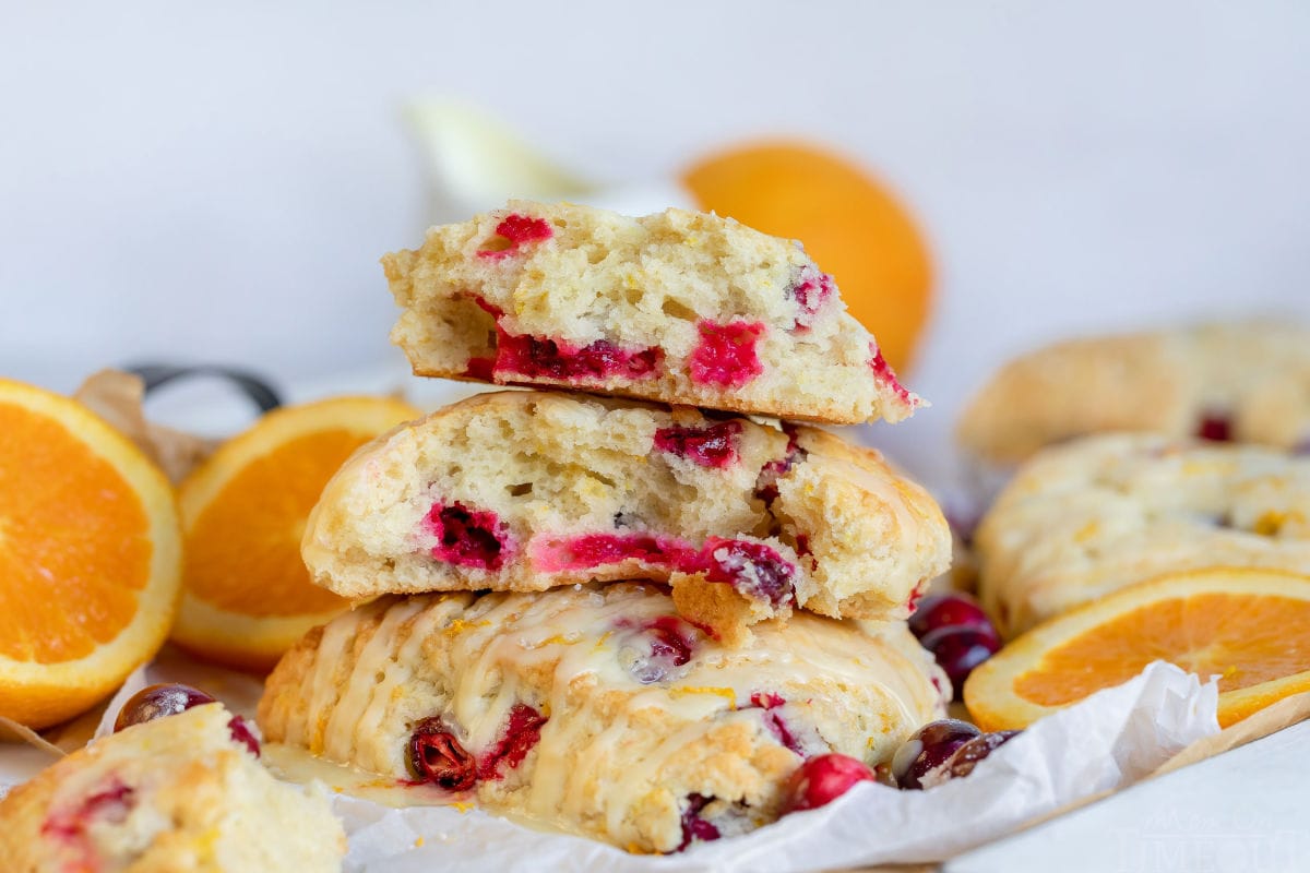 cranberry orange scones split up and sitting on parchment paper with orange slices and cranberries scattered about