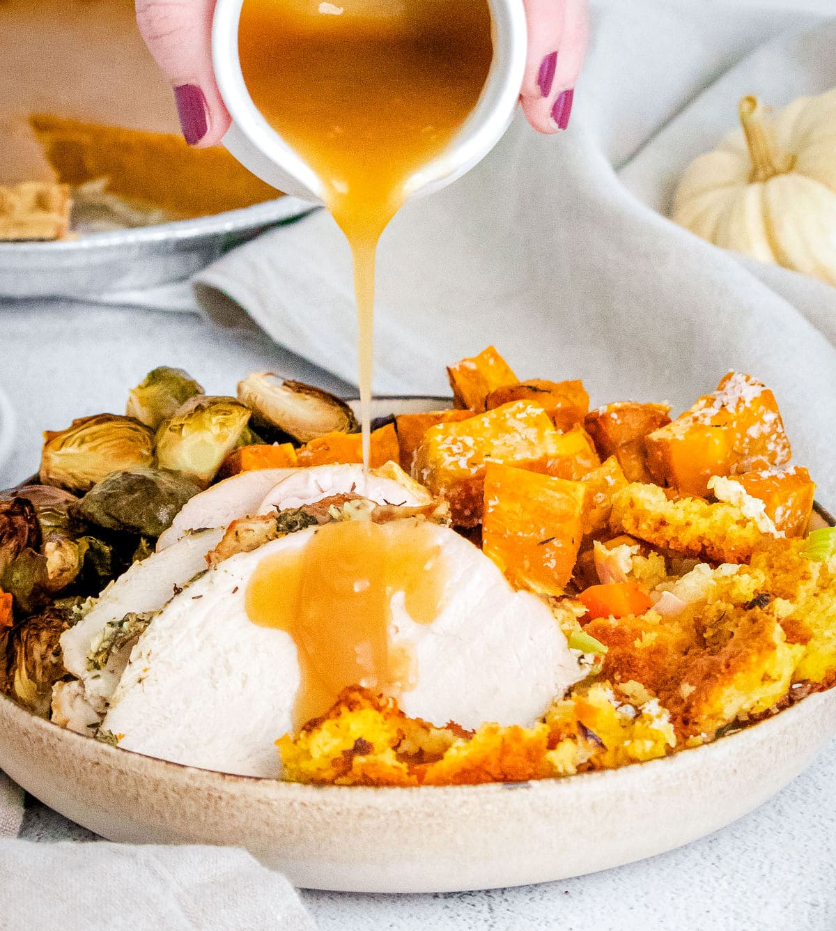 gravy being poured on roast turkey on a plate with side dishes and pie in the background