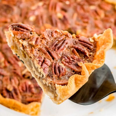 slice of pecan pie on pie server with whole pie beneath
