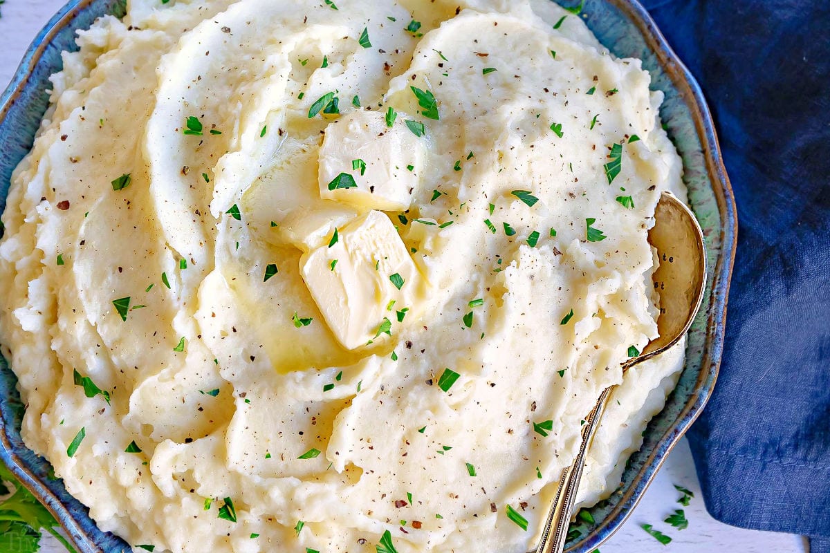 top down close up look at mashed potato recipe in a shallow bowl with butter and parsley.