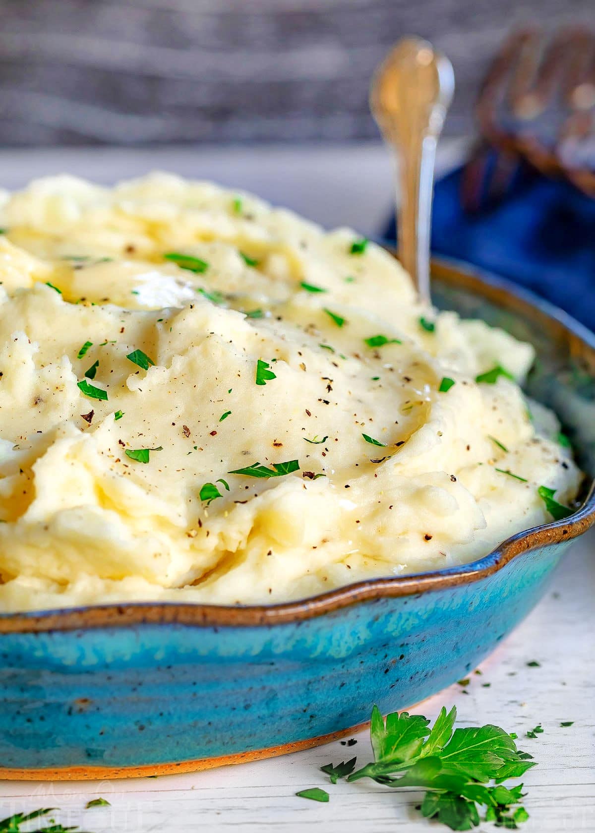 front view of large blue bowl of creamy mashed potato recipe topped with fresh parsley and butter.