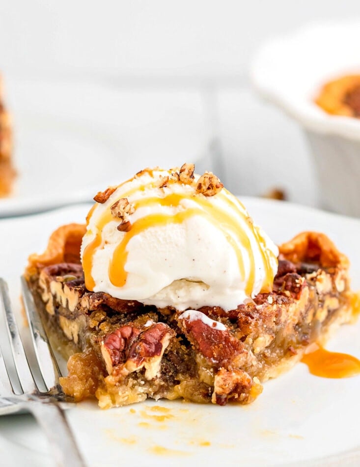 pecan pie slice on plate with bite taken topped with ice cream and caramel sauce